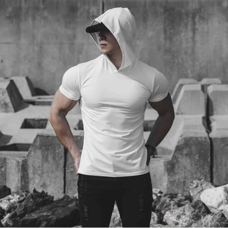 Person wearing a white hoodie and black pants standing against a concrete wall.